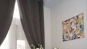 Une pièce comprenant une chaise blanche, une table d’appoint blanche ornée d’un vase de fleurs, un canapé noir et un mur sur lequel est accrochée une peinture abstraite aux couleurs vives.