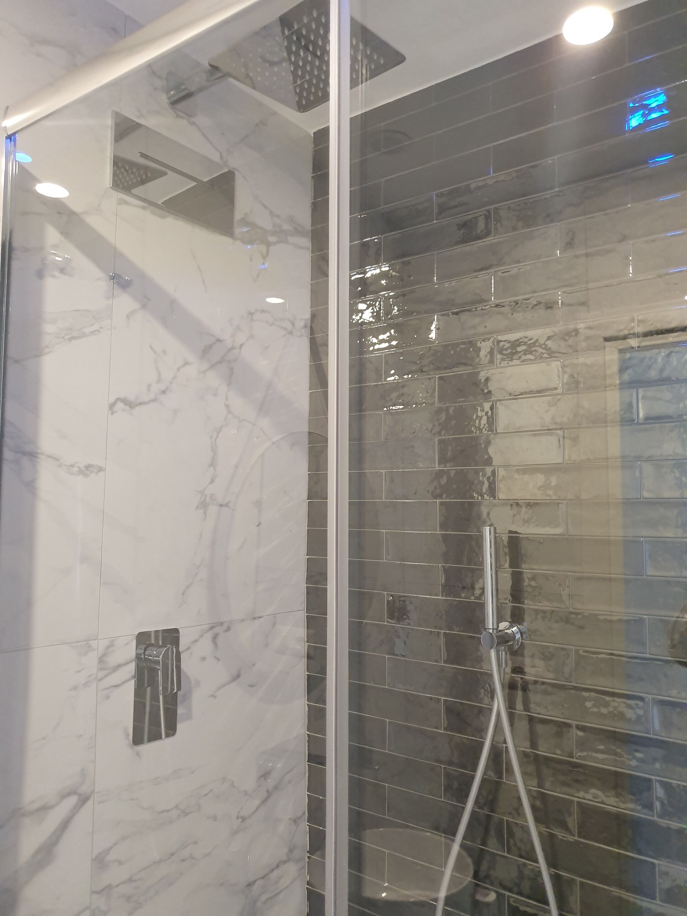 A shower with a glass door, marble walls, and a tiled shower area.