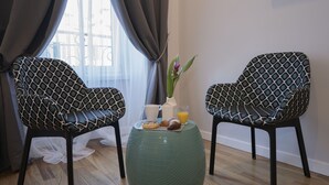 Deux chaises à motifs, une petite table avec un vase et un croissant, et une fenêtre avec des rideaux.