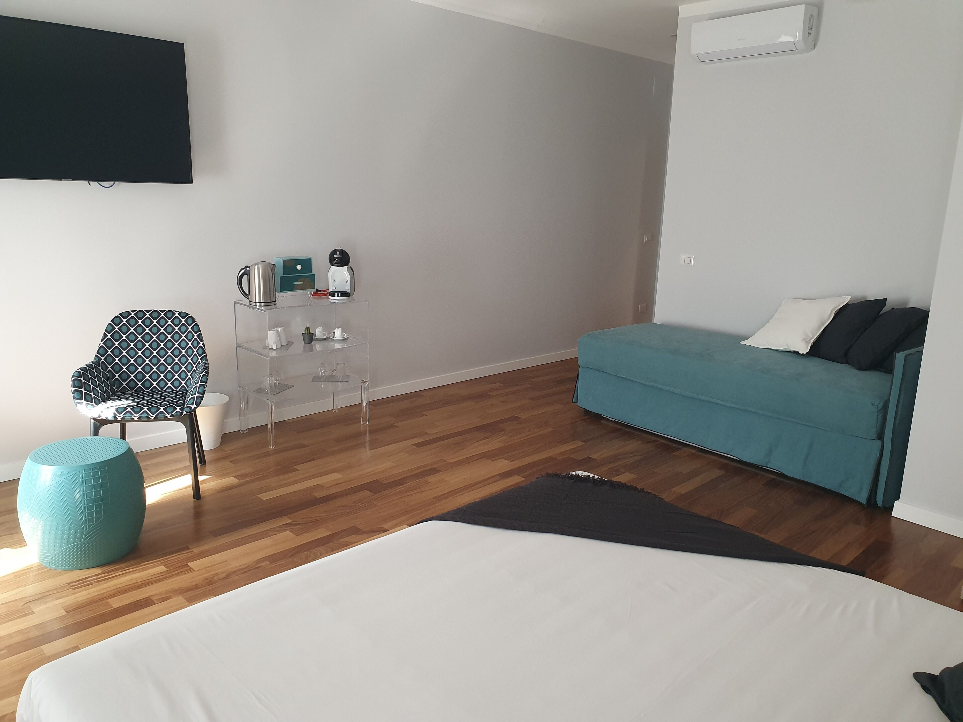 A modern hotel room with a bed, a sofa, a chair, a coffee table, and a TV mounted on the wall.