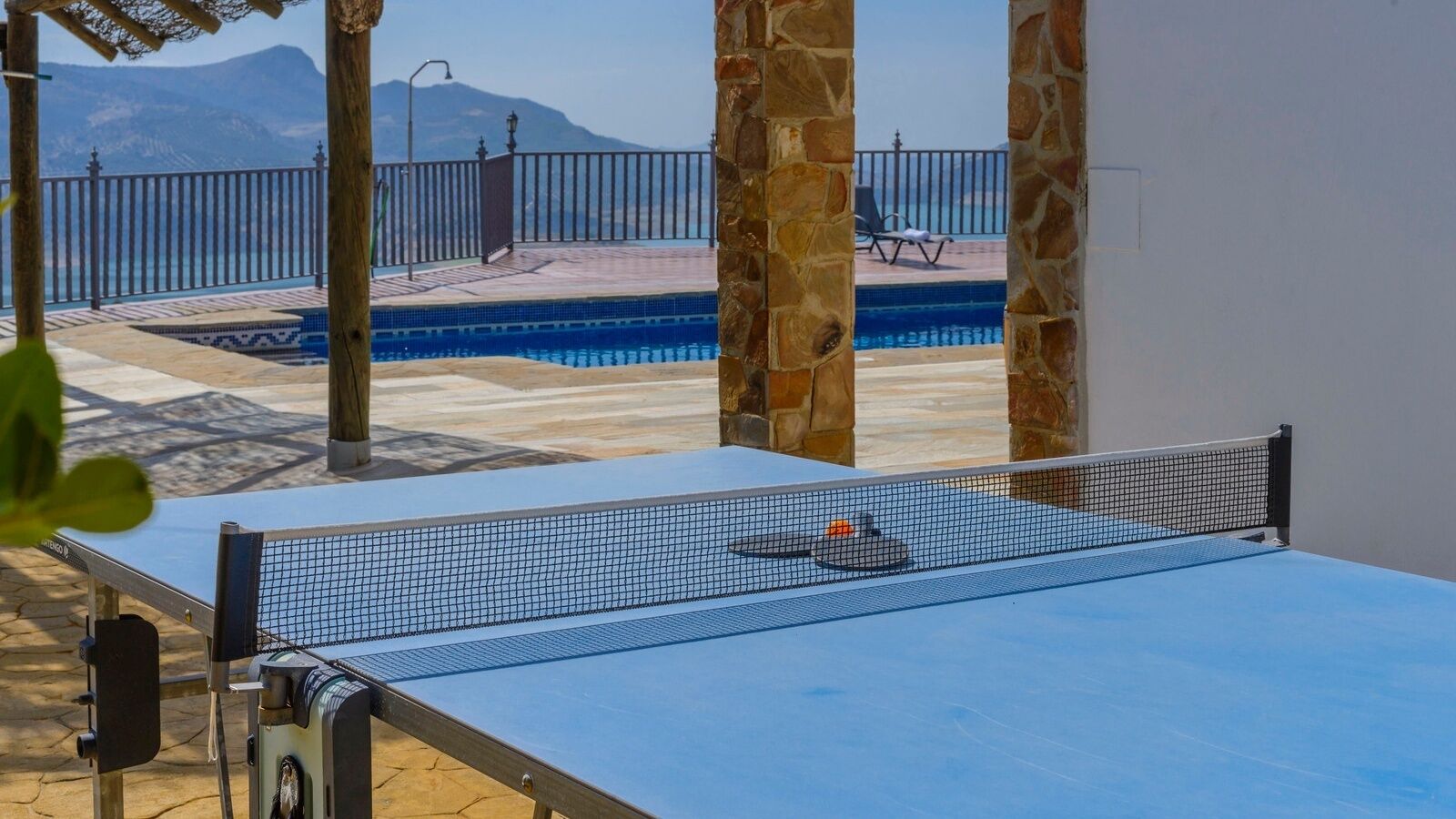 A ping pong table with a net, a pool, and a stone wall in the background.