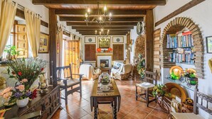 A cozy room with a wooden ceiling, a fireplace, a dining table, and a bookshelf filled with books. - Las Monjas - Camara Periana by Ruralidays (Málaga)