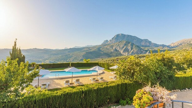 A pool area with lounge chairs and umbrellas, surrounded by greenery and mountains in the background. - Las Monjas - Camara Periana by Ruralidays (Málaga)