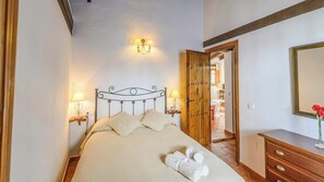 Una cama bien hecha con cabecera de metal, dos lámparas de noche y una puerta de madera que da a otra habitación.