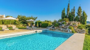 Una piscina rectangular con agua azul cristalina, rodeada por un muro de piedra y abundante vegetación.