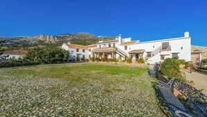 A white building with a tiled roof, a cobblestone courtyard, and a mountain in the background. - Las Monjas - Camara Periana by Ruralidays (Málaga)