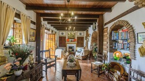 A cozy room with a wooden ceiling, a fireplace, a dining table, and a bookshelf. - Las Monjas - Saladero Periana by Ruralidays (Málaga)