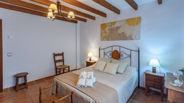 A bedroom with a bed, a chair, a nightstand, a lamp, and a painting on the wall. - Las Esparragueras Cómpeta by Ruralidays (Málaga)