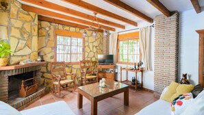 A rustic living room with stone walls, wooden furniture, a fireplace, and a television. - Las Esparragueras Cómpeta by Ruralidays (Málaga)