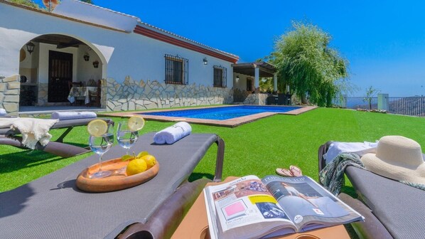 Un espace aménagé au bord de la piscine, avec des chaises longues, une table sur laquelle se trouve un plateau de citrons et des verres, ainsi qu’un magazine.