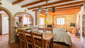 A rustic kitchen with stone walls, wooden beams, and a dining area with a table and chairs. - Las Esparragueras Cómpeta by Ruralidays (Málaga)
