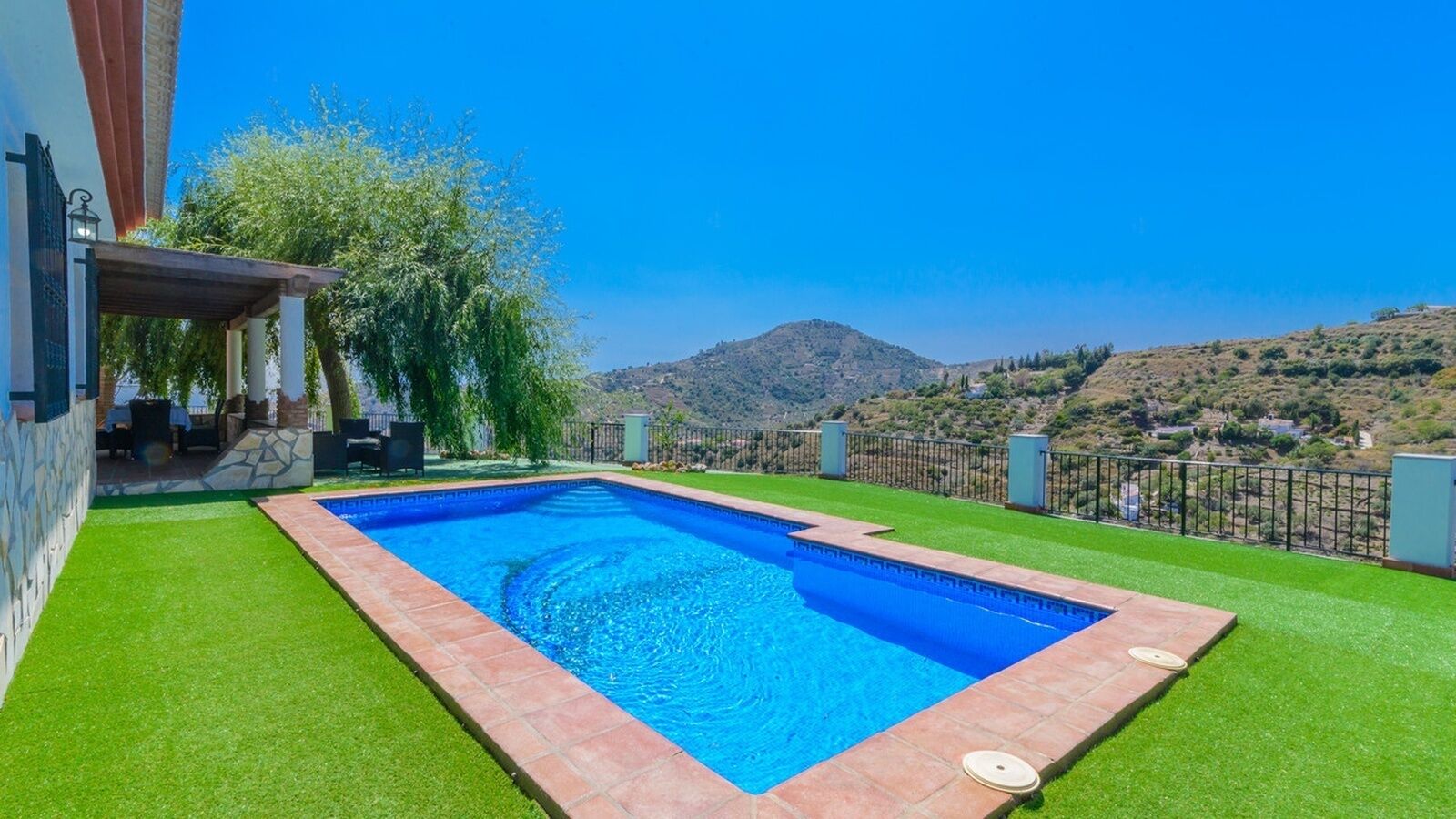 A rectangular swimming pool with a clear blue water, surrounded by green artificial grass, and a stone border.