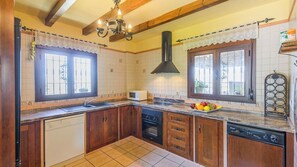 A kitchen with wooden cabinets, a stove, a microwave, and a fruit bowl on the counter. - La Meica Alcaucín by Ruralidays (Málaga)