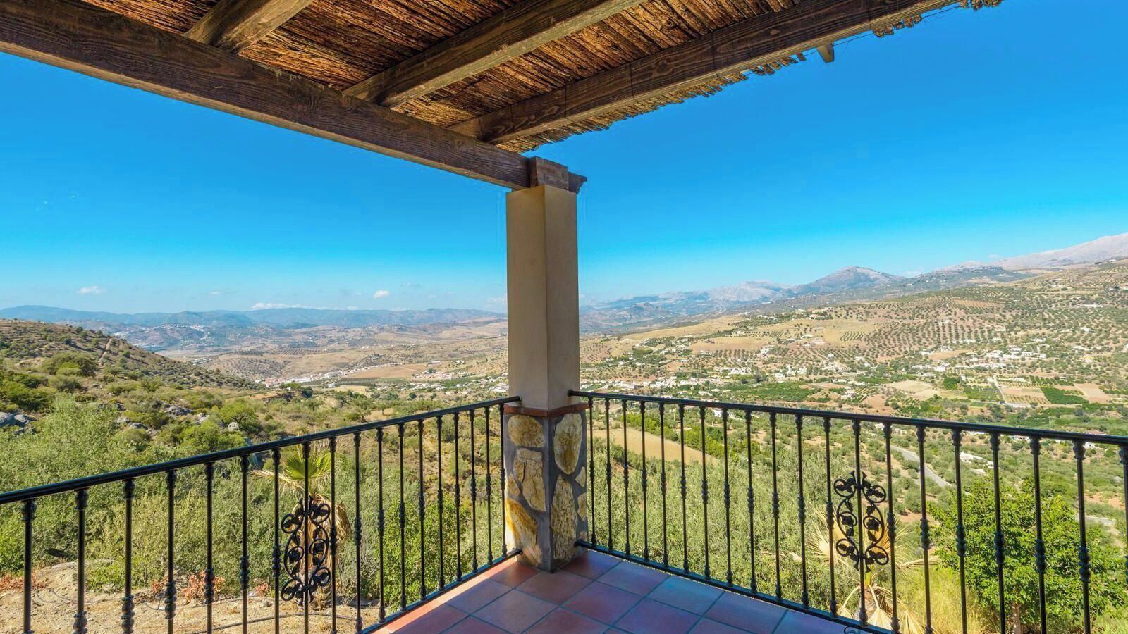 A balcony with a metal railing overlooking a valley with scattered buildings and greenery.