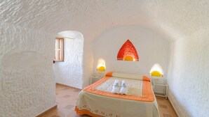 A bedroom with a bed, two bedside lamps, a window, and a textured wall. - Cuevas La Chumbera - Casa La Higuera 4pax Fonelas by Ruralidays (Granada)