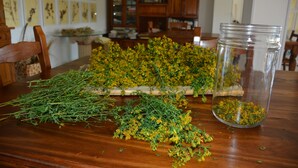 Une table en bois, parsemée d’herbes séchées, et un bocal en verre.