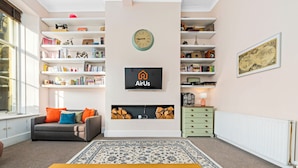 A living room with a sofa, a coffee table, a bookshelf, a fireplace, and a clock on the wall. - Vibrant Spacious Apartment In West End (Glasgow)