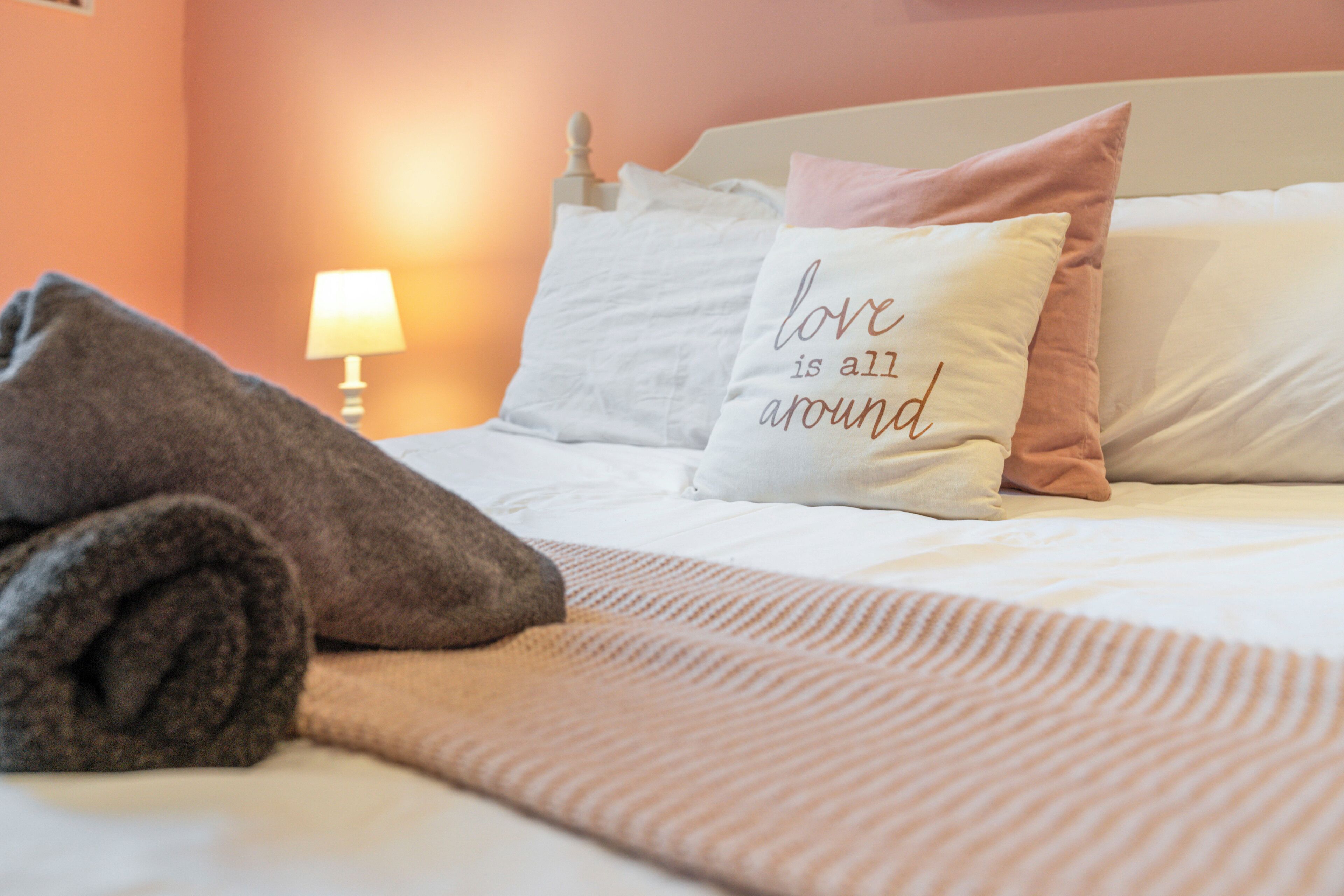 A neatly made bed with pillows, a rolled towel, and a lamp in the background.