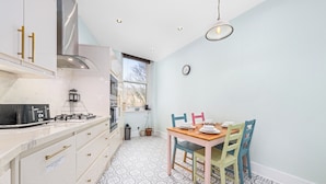 A modern kitchen with a gas stove, white cabinets, and a dining area with a wooden table and chairs. - Vibrant Spacious Apartment In West End (Glasgow)