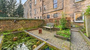 A courtyard with a bench, a small pond, and a brick wall. - Vibrant Spacious Apartment In West End (Glasgow)