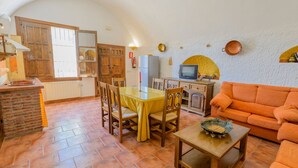 A cozy living room with a wooden table and chairs, a sofa, and a television. - Cuevas La Chumbera - Jazmines 9pax Fonelas by Ruralidays (Granada)