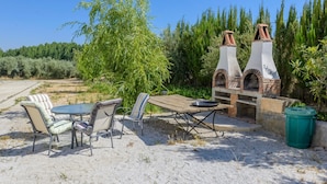 An outdoor dining area with a table and chairs, a brick oven, and surrounding greenery. - Cuevas La Chumbera - Jazmines 9pax Fonelas by Ruralidays (Granada)