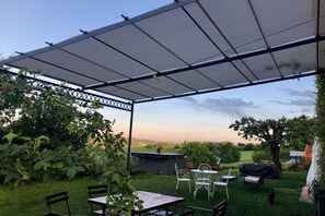 Un patio exterior con zona de estar cubierta, una parrilla y vistas al campo.