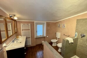 Un baño con lavamanos, dos inodoros, una ventana y zona de ducha.