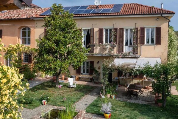 Una casa de dos pisos con jardín, balcón y paneles solares en el techo.