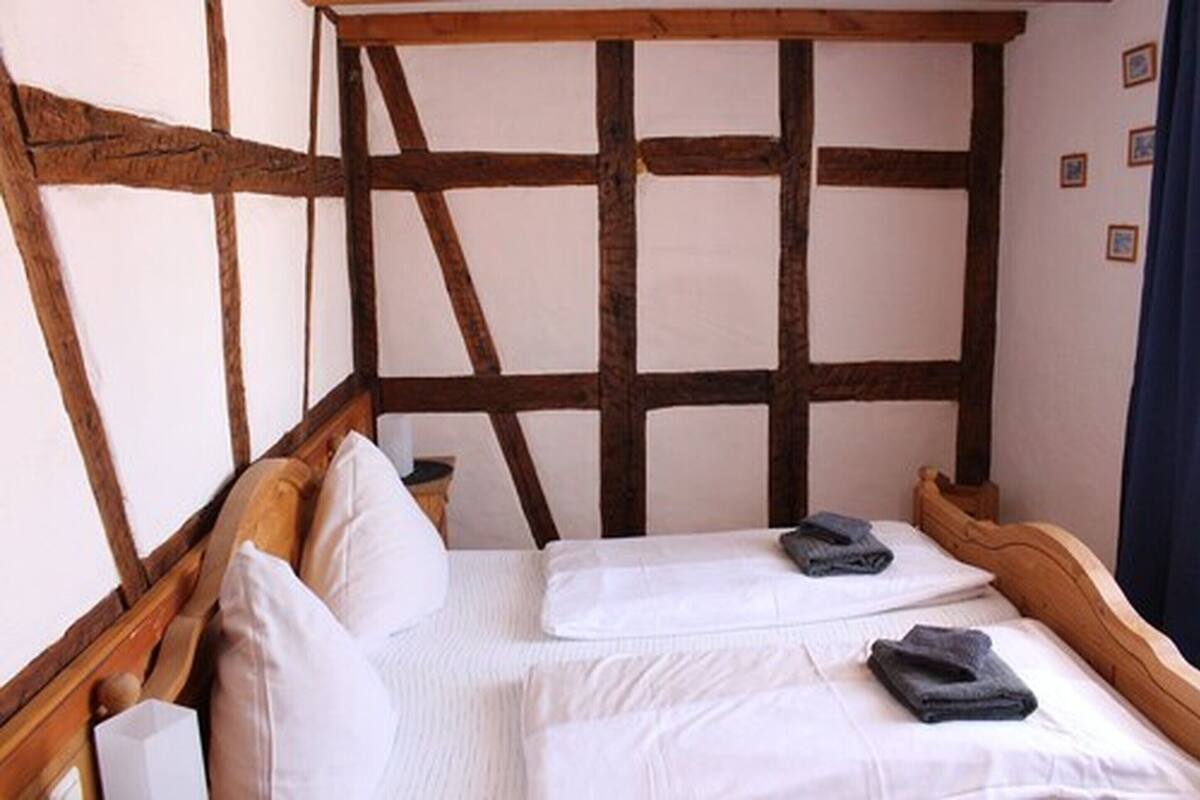 A room with a simple bed, white linens, and a wooden headboard.