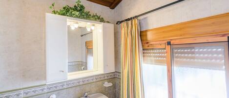 A bathroom with a sink, mirror, and shower area.