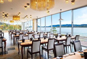 A restaurant with large windows offering a view of a lake and mountains. Tables are set with chairs and dining ware. - The Gran Resort Amanohashidate (Miyazu)