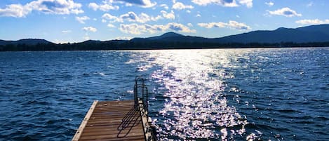 Une jetée en bois s’étendant sur un lac paisible, avec un ciel dégagé et des montagnes en arrière-plan.