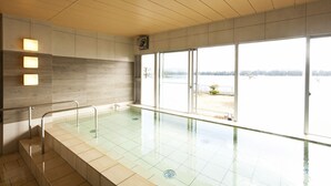 A modern indoor swimming pool with clear glass walls, a wooden ceiling, and a view of a distant landscape. - The Gran Resort Amanohashidate (Miyazu)