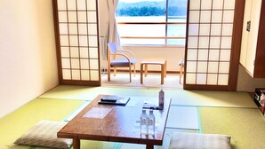 A tatami mat room with a wooden table, two pillows, a chair, and a view through shoji screens. - The Gran Resort Amanohashidate (Miyazu)