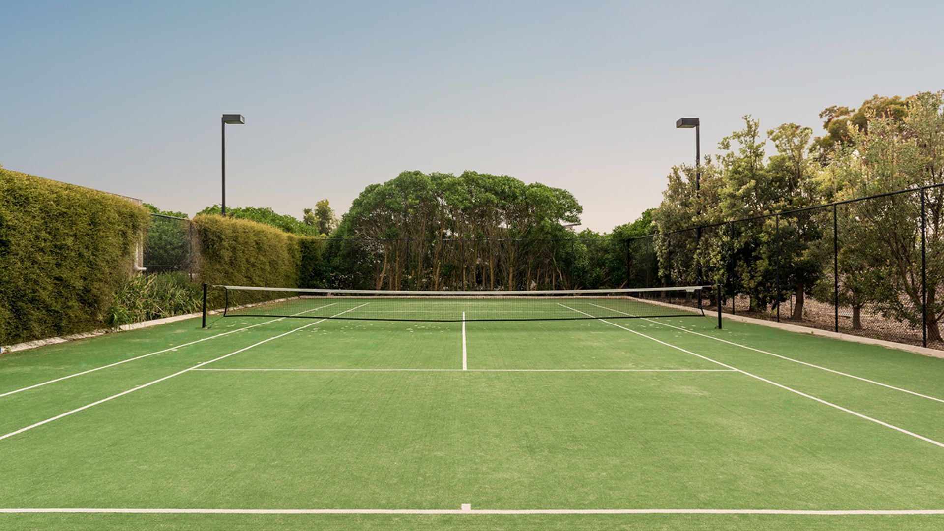 A tennis court with a net, surrounded by trees and hedges.