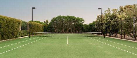 A tennis court with a net, surrounded by trees and hedges.