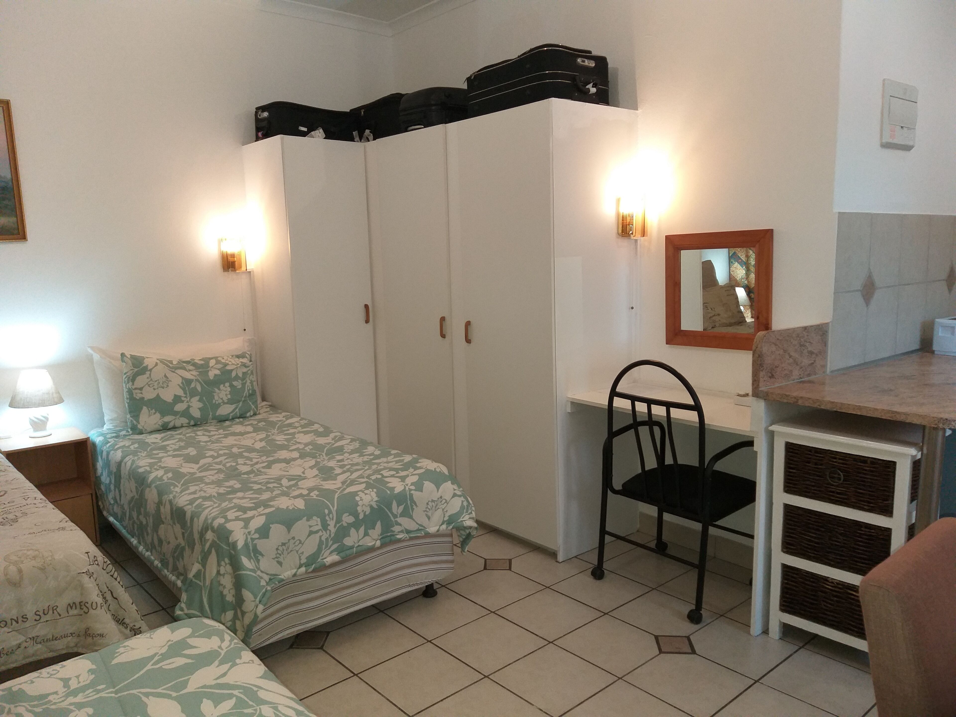 A bedroom with a bed, wardrobe, desk, chair, and a small table.