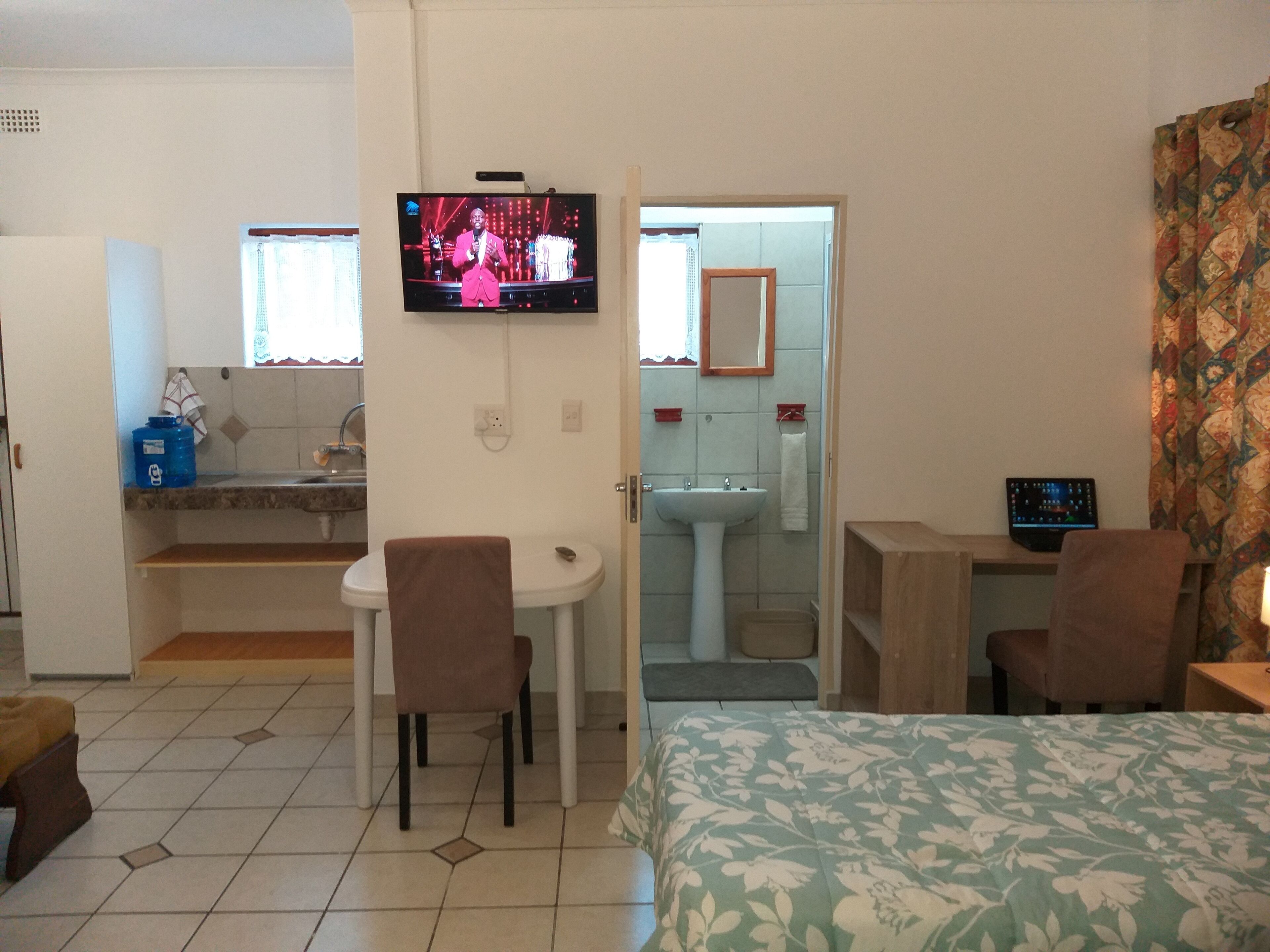 Ein Hotelzimmer mit einem Bett, einem Schreibtisch, einem Stuhl, einem Fernseher, einem Waschbecken und einem Spiegel.
