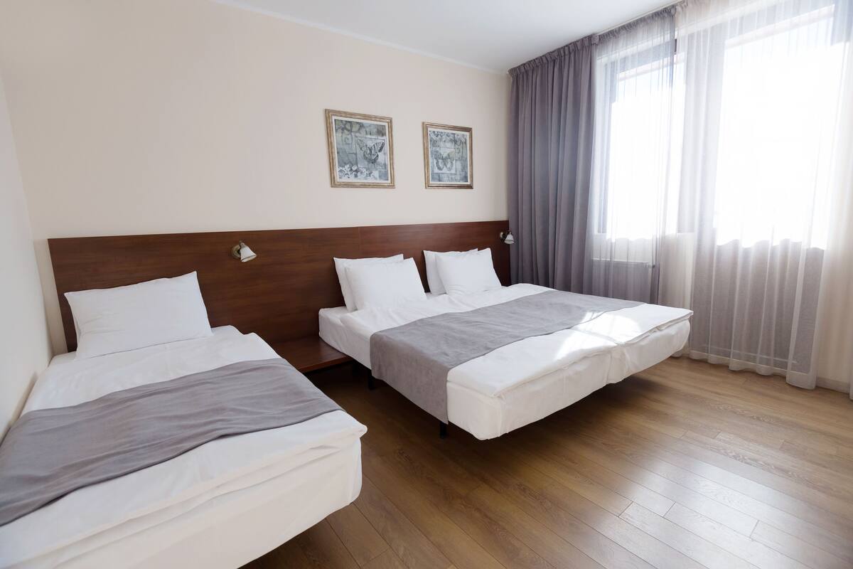 A hotel room with two beds, a wooden headboard, and a large window with curtains.