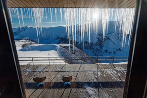 A wooden deck with two wicker chairs, overlooking a snowy mountain landscape with icicles hanging from the ceiling. - Hotel Monte Gudauri (Kazbegi)
