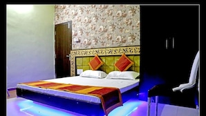A bed with a headboard, a chair, and a wall with floral wallpaper. - Hotel Shri Karani Vilas (Chittorgarh)