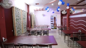 A restaurant with multiple tables and chairs, ceiling fans, and decorative balloons. - Hotel Shri Karani Vilas (Chittorgarh)