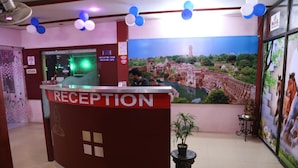 A reception area with a red counter, a large window, and a mural of a historical building. - Hotel Shri Karani Vilas (Chittorgarh)