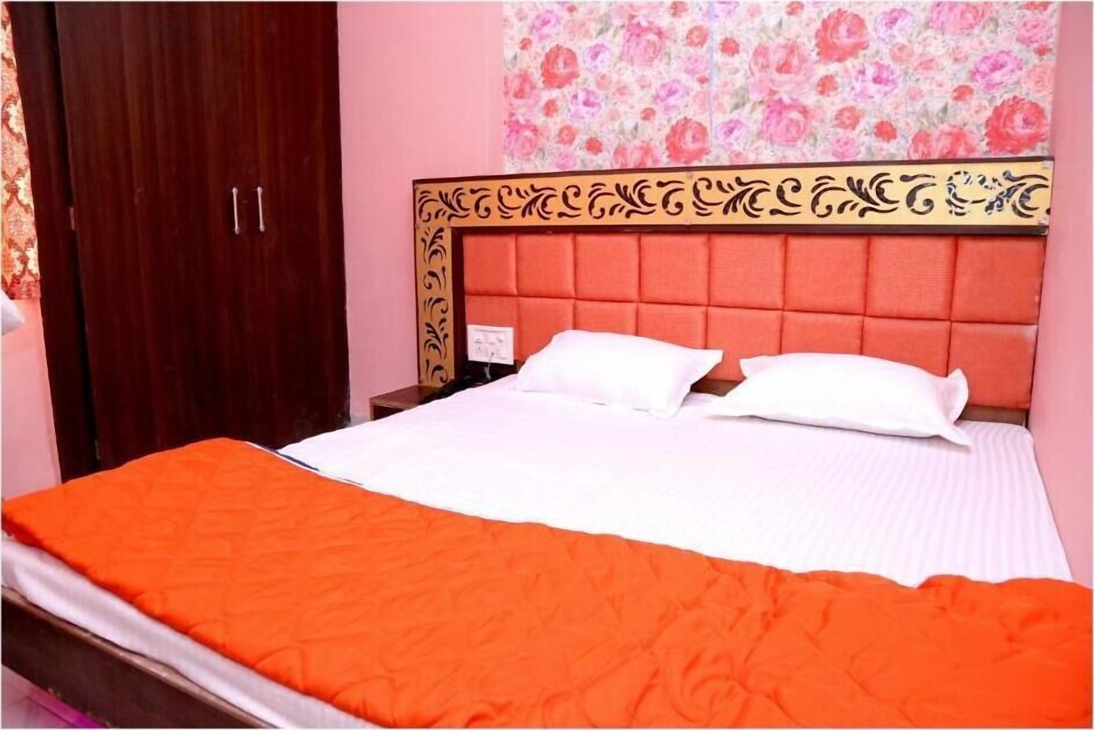 Uma cama com colcha laranja, um guarda-roupa de madeira e papel de parede floral.
