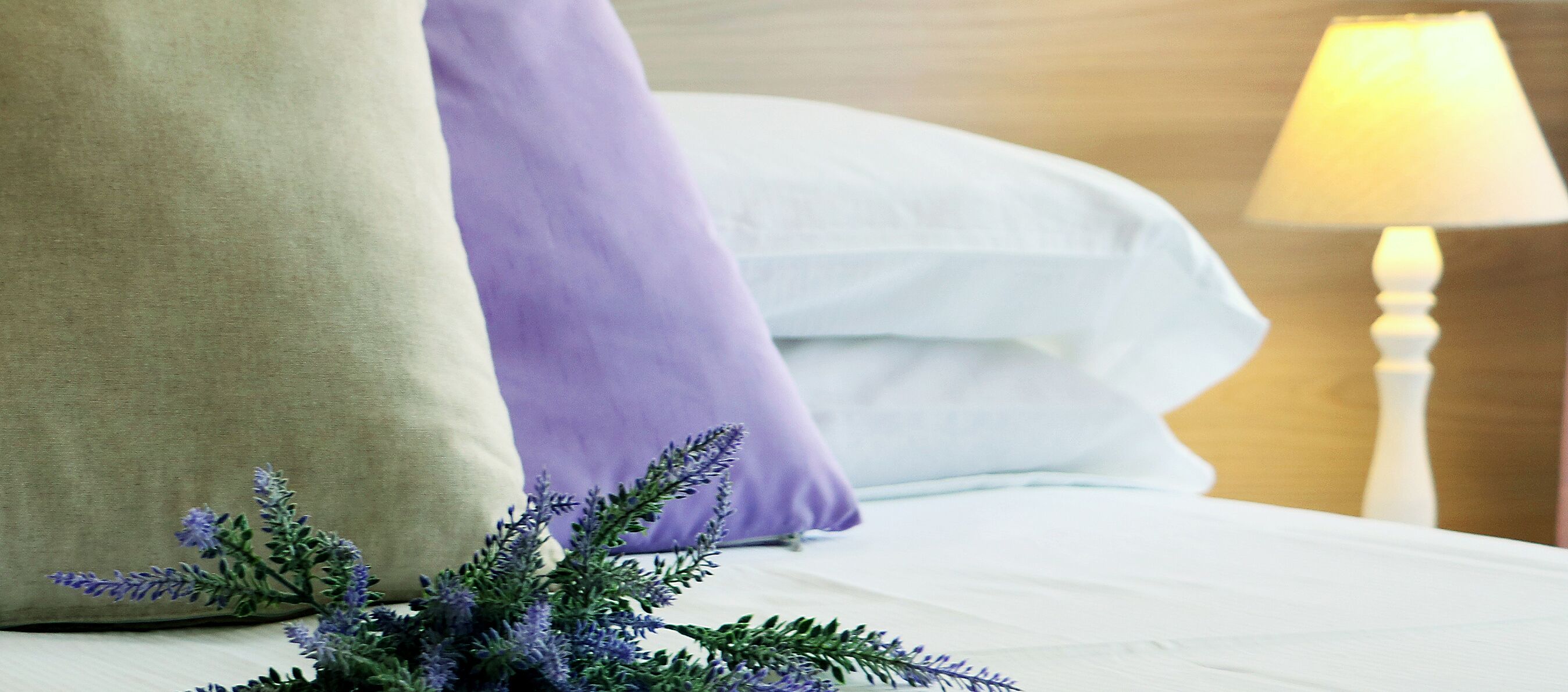 A neatly made bed with white linens, a beige pillow, and a purple pillow.