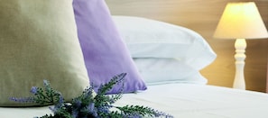 Een netjes opgemaakt bed met witte lakens, een beige kussen en een paars kussen.