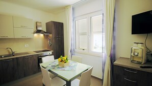 A compact kitchen with a dining area, a built-in oven, a sink, and a window with blinds.