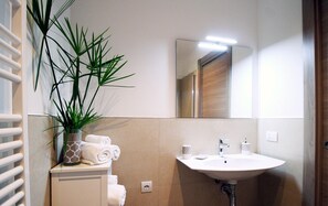 Een badkamer met een wit wastafel, een spiegel, een handdoekhouder en een potplant.