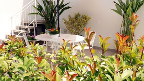 A patio area with a round table and chairs, surrounded by various plants and a staircase.